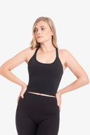 Mujer joven con top negro sin mangas y pantalones deportivos negros, fondo blanco