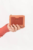 Mano con suéter naranja sosteniendo cartera pequeña MOIXX de cuero en tonos rosa y marrón