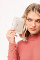 Mujer rubia con suéter rosa sosteniendo carterá blanca Moxx cerca del rostro en fondo blanco